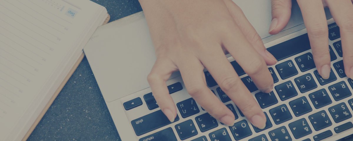 Hands Typing on a Laptop Keyboard with a Notepad and Pen