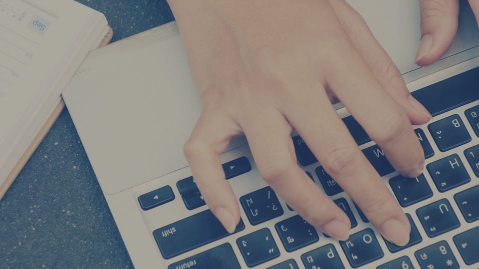 Hands Typing on a Laptop Keyboard with a Notepad and Pen